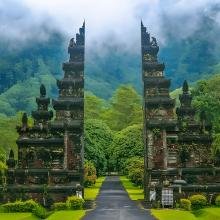 Majestic Balinese stone gate stands tall amid lush greenery and misty mountains, conveying serenity and mysticism in a tropical landscape.