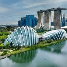 A futuristic cityscape with distinctive architecture; curved glass buildings by a lush green park and calm water, with skyscrapers in the background.