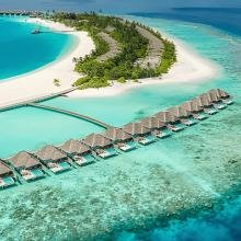 Aerial view of a tropical island with overwater bungalows, lush greenery, and white sandy beaches surrounded by clear turquoise waters, conveying serenity.