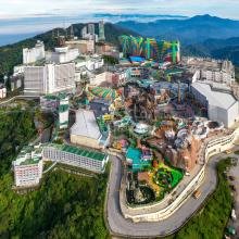 Aerial view of a vibrant, colorful theme park nestled in lush green mountains. Hotels and attractions dot the landscape, exuding a lively, adventurous vibe.