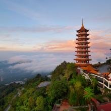 A serene landscape features a multilevel pagoda against a backdrop of lush hills and soft clouds at sunset, conveying tranquility and beauty.
